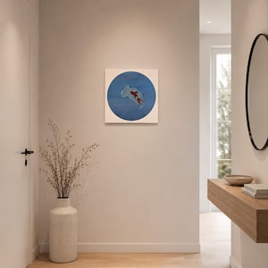 Könnte beinhalten: Ein quadratisches Wandbild mit einem kreisförmigen blauen Hintergrund und einer Illustration eines roten Koi-Fisches in der Mitte der Leinwand. Das Kunstwerk hängt an einer schlichten Wand in einem Flur über einer Bodenvase mit dünnen Zweigen.
