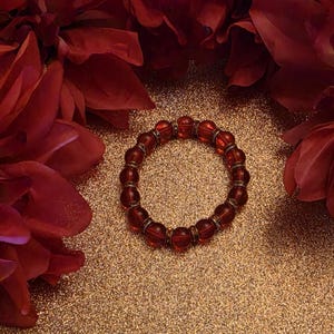 May include: A circular stretch bracelet composed of translucent deep red glass beads alternating with smaller, metallic-toned spacer beads featuring a textured, ridged design. The beads are arranged in a repeating pattern around the entire circumference.