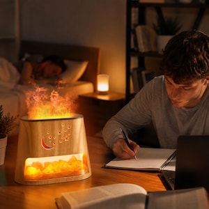 Può includere: Un diffusore di oli essenziali con finitura effetto legno chiaro, base rettangolare e una finestra trasparente che mostra rocce di sale arancioni luminose. La parte superiore emette un effetto fiamma simulato e il frontale presenta un design ritagliato a forma di mezzaluna e stelle.