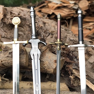 Op de afbeelding: Vier metalen zwaarden naast elkaar. Het eerste heeft een gouden pommel en stootplaat. Het tweede heeft een ingewikkeld zilveren gevest met een centraal ontwerp. Het derde heeft een bronskleurige stootplaat en een donkerrode greep. Het vierde is zwart.