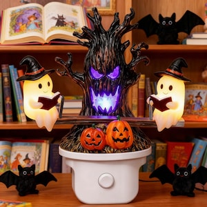 Puede incluir: Una luz nocturna con temática de Halloween que presenta un árbol oscuro y nudoso con ojos y boca de color púrpura brillante, flanqueado por dos fantasmas iluminados con sombreros de bruja negros leyendo en un balancín, con dos calabazas naranjas.
