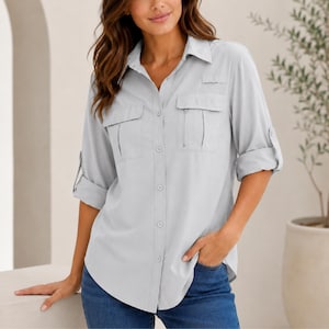 Puede incluir: Una camisa de botones gris claro con cuello clásico, mangas largas con pestañas para enrollar y dos bolsillos en el pecho con solapas. La camisa está confeccionada con una tapeta central de botones y un dobladillo curvo funcional.