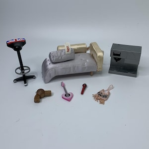 May include: A miniature doll furniture set including a black bar stool with a Union Jack seat, a light purple chaise lounge with a Bratz tag, a gray coffee machine, a brown hair dryer, a pink heart-shaped guitar, a red microphone, and a small bag.