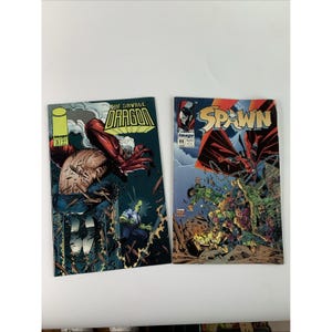 May include: Two comic books from Image Comics. The left cover is The Savage Dragon issue 3, featuring a red-skinned character. The right cover is Spawn issue 11, showing a caped figure with chains above a chaotic scene of green-clad soldiers.
