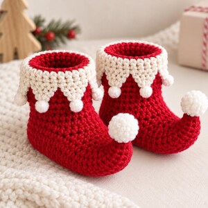 Peut inclure: Une paire de chaussons en crochet rouge avec un bout retroussé et un pompon blanc à l'extrémité. Les bords de cheville présentent une bordure festonnée blanche avec de petits pompons blancs attachés à chaque pointe, créant un aspect festif.