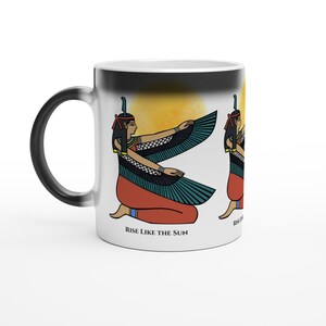 Peut inclure: Un mug en céramique blanc avec un dégradé noir sur le haut, illustré d'une figure égyptienne ailée agenouillée devant un soleil jaune. Le personnage porte un vêtement rouge et une coiffe bleue. Le texte RISE LIKE THE SUN est inscrit en dessous.