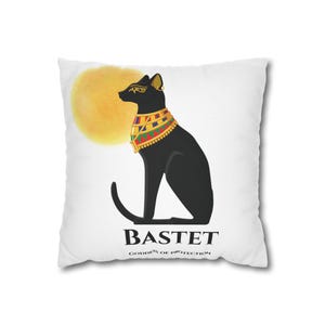 Peut inclure: Un coussin carré blanc orné d'une silhouette noire de chat égyptien portant un collier de perles colorées et des bijoux dorés. Derrière le chat se trouve un cercle jaune. Sous le chat, le texte indique BASTET GODDESS OF PROTECTION.