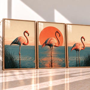 Può includere: Un set di tre stampe artistiche da parete incorniciate raffiguranti fenicotteri rosa in piedi nell'acqua blu. La stampa centrale mostra un grande sole arancione dietro un fenicottero. Ogni stampa presenta erba alta e un cielo dai toni caldi.