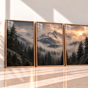 May include: A triptych of three framed wall art prints featuring a continuous mountain landscape. The scene depicts snow-capped peaks, dense evergreen forests, and low-hanging mist under a golden sunset sky, all encased in thin gold frames.