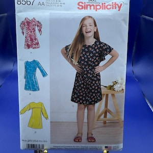 May include: A Simplicity sewing pattern envelope 8567 for sizes 8-16, featuring illustrations of four dress variations: a red floral dress, a blue patterned dress, a black floral dress, and a solid yellow dress with long sleeves.