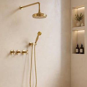 May include: A bathroom featuring a gold shower system with a wall-mounted showerhead and a handheld sprayer, three gold cross-handle valves, a gold wall-mounted faucet, a vessel sink, an oval mirror, and two gold wall sconces on a beige wall.