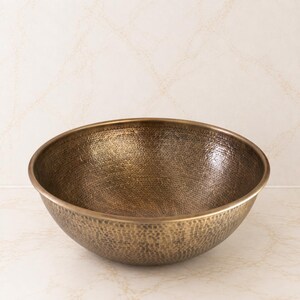May include: A round, deep basin with a hammered texture and a metallic bronze finish. The bowl features a smooth, rounded rim and a consistent, dark, antique-toned surface throughout the interior and exterior, showcasing a handcrafted appearance.