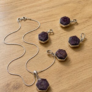 May include: A silver chain necklace with a hexagonal purple gemstone pendant and four additional matching hexagonal purple gemstone pendants, each set in a silver frame with a small metal loop for attachment to a chain or cord.
