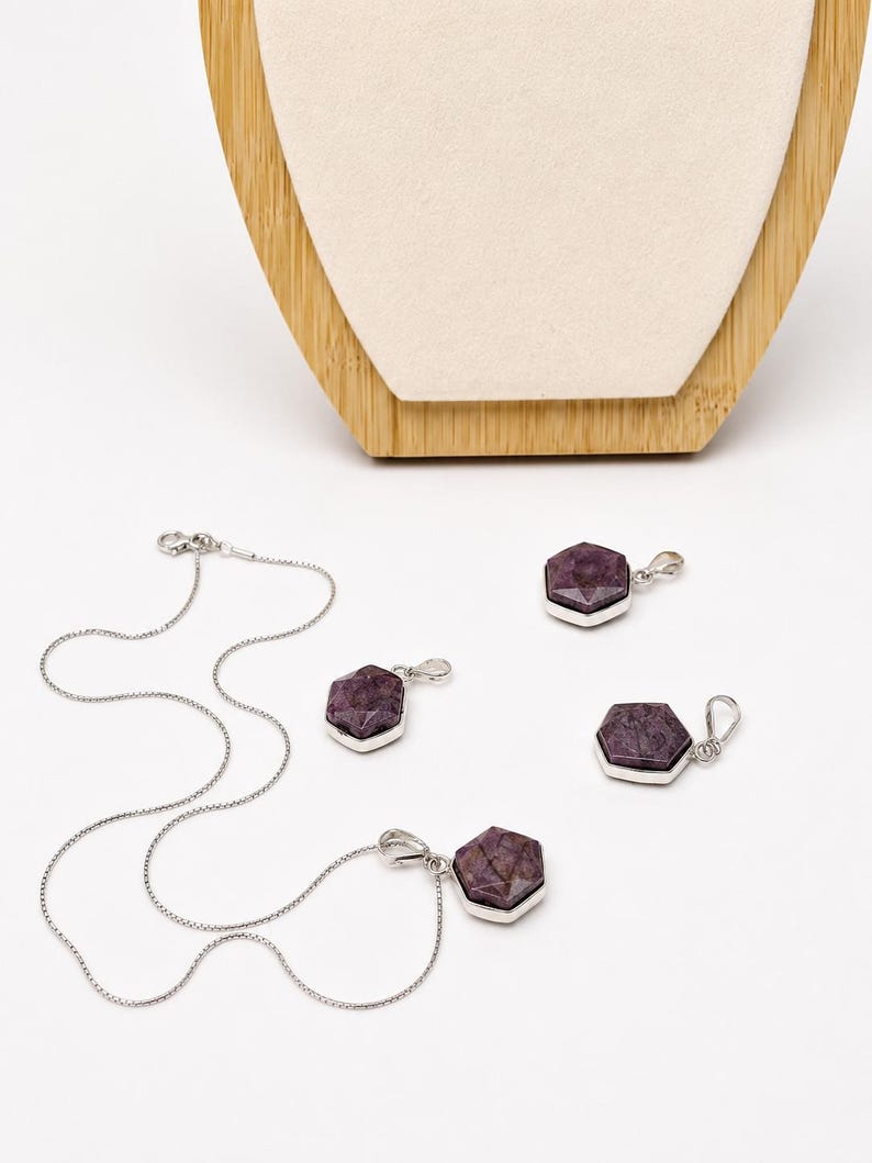 May include: A jewelry set consisting of a silver chain necklace and three matching pendants. Each pendant features a faceted, hexagonal, deep purple stone set in a polished silver frame. The necklace includes a delicate silver chain with a clasp.