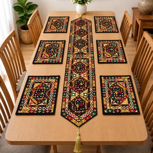 May include: A rectangular table runner and six matching rectangular placemats featuring a geometric pattern in black, red, green, and yellow. The runner has a pointed end with a light gold tassel. Each piece is bordered in black fabric.