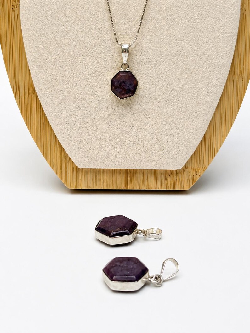 May include: A silver necklace featuring a hexagonal dark purple gemstone pendant, accompanied by two matching hexagonal dark purple gemstone pendants with silver bails, each displaying a faceted surface and a polished metallic setting.