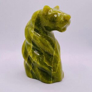 May include: A polished green stone sculpture of a feline animal in a seated position. The carving features deep olive and lime green colour variations with a smooth, glossy finish and distinct natural veining throughout the entire surface.