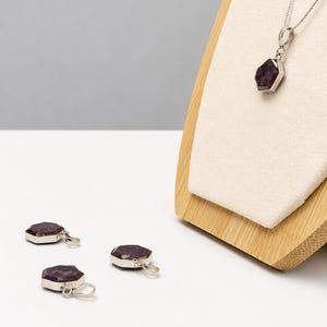 May include: A silver necklace featuring a hexagonal dark purple gemstone pendant on a thin chain, accompanied by two matching loose hexagonal dark purple gemstone pendants with silver bails, all displaying a faceted surface and metallic settings.