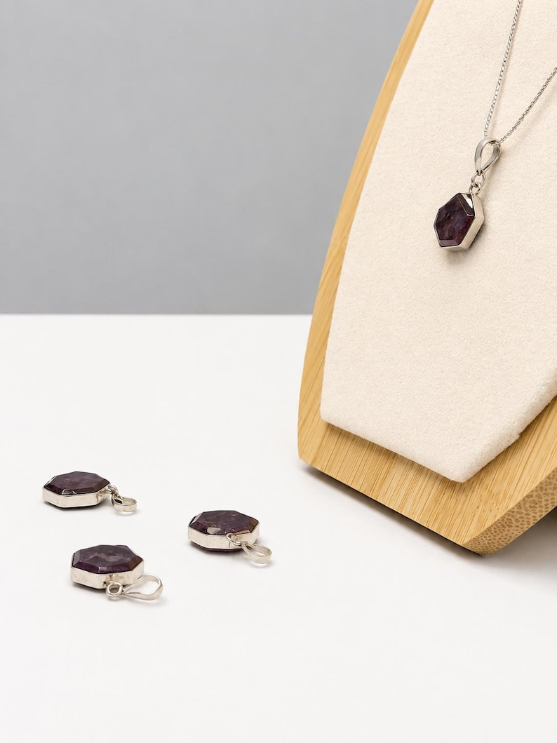 May include: A silver necklace featuring a hexagonal dark purple gemstone pendant on a thin chain, accompanied by two matching loose hexagonal dark purple gemstone pendants with silver bails, all displaying a faceted surface and metallic settings.