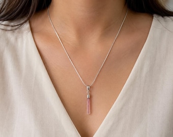 May include: A silver chain necklace featuring a slender, vertical, translucent pink crystal pendant. The pendant is capped with a polished silver metal bail that connects it to the delicate, textured silver chain resting against the neck.