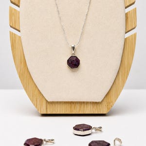 May include: A silver necklace featuring a faceted, octagonal dark purple gemstone pendant. Three additional matching octagonal gemstone pendants with silver bails are arranged below the necklace, each displaying a deep plum-colored surface.