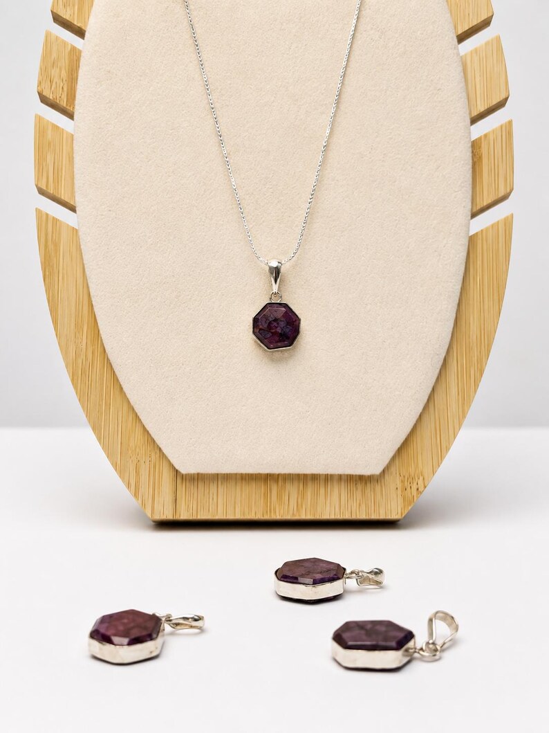 May include: A silver necklace featuring a faceted, octagonal dark purple gemstone pendant. Three additional matching octagonal gemstone pendants with silver bails are arranged below the necklace, each displaying a deep plum-colored surface.