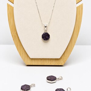 May include: A silver necklace featuring a faceted, dark purple, octagonal pendant on a thin chain, accompanied by three matching loose silver pendants with the same dark purple, faceted, octagonal stone design, all displayed together.