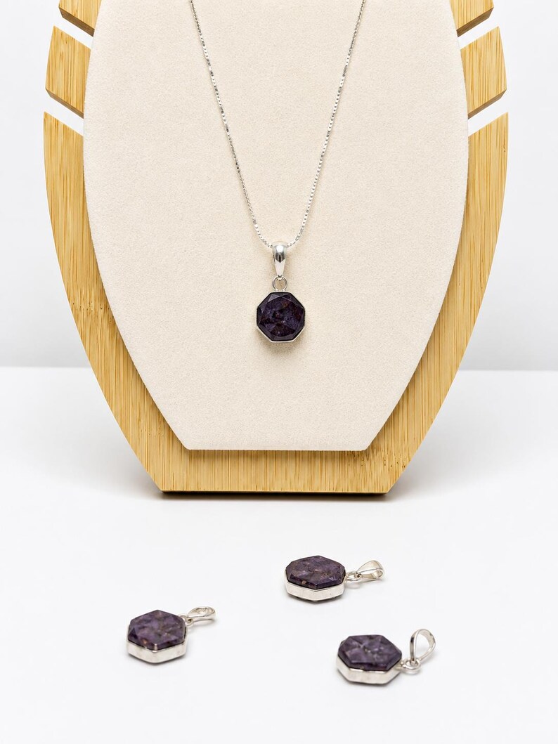 May include: A silver necklace featuring a faceted, dark purple, octagonal pendant on a thin chain, accompanied by three matching loose silver pendants with the same dark purple, faceted, octagonal stone design, all displayed together.