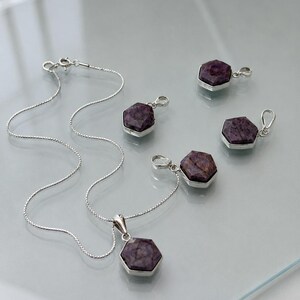 May include: A silver necklace with a hexagonal purple gemstone pendant and four matching hexagonal purple gemstone charms, each set in a silver frame with a small silver bail for attachment, featuring a delicate silver chain with a spring ring clasp.