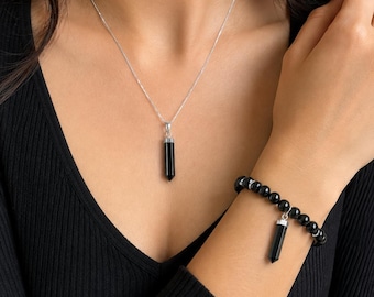 May include: A silver chain necklace with a black stone point pendant and a matching stretch bracelet featuring black spherical beads and a single black stone point charm, both set in silver-toned metal, worn with a black ribbed long-sleeve top.