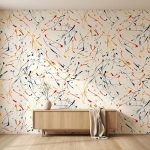 May include: A light-colored wall covered in wallpaper featuring a pattern of abstract paint splatters in shades of dark blue, orange, and yellow. A light wood console table sits against the wall, topped with a small vase containing bare twigs.