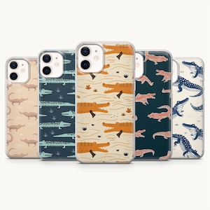 Può includere: Cinque cover trasparenti per smartphone disposte in fila, ognuna caratterizzata da un distinto motivo ripetitivo di coccodrilli. I design includono varie combinazioni di colori come arancione, blu scuro, azzurro e crema, con illustrazioni stilizzate di alligatori.