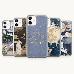 May include: Five clear smartphone cases featuring various illustrations of rabbits, stars, and moons. The designs include rabbits in a circle on a blue background, rabbits near a large moon, and rabbits amidst floral elements and clouds in dark tones.