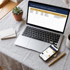 May include: A silver laptop displaying a spreadsheet titled CLIENT RELATIONSHIPS & REFERRALS, a smartphone showing a calendar app, a gold pen, a ceramic mug with dark liquid, a small potted succulent, and a stack of blank white cards.
