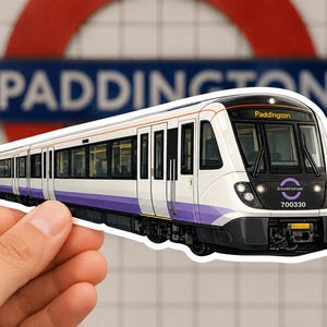 Op de afbeelding: Een gestanste sticker van een witte en paarse Elizabeth Line-trein met de tekst Paddington op het bestemmingsdisplay en 700330 aan de voorzijde. De trein heeft een strak modern ontwerp met zwarte raamkozijnen en een donkere neus.