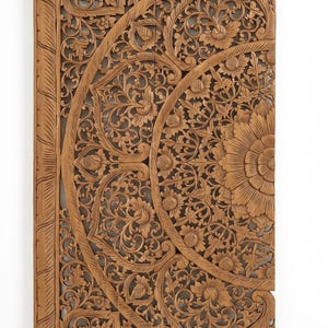 K&ouml;nnte beinhalten: Ein rechteckiges Wandpaneel aus hellbraunem Holz mit detaillierten, handgeschnitzten Blumen- und Blattmotiven. Das Design zeigt ein gro&szlig;es, zentrales kreisf&ouml;rmiges Muster mit geschichteten Bl&uuml;tenbl&auml;ttern und Ranken, umrahmt von einer geraden Bord&uuml;re mit seilartiger Struktur.
