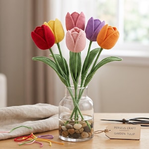 May include: A bouquet of six crocheted tulips in red, yellow, pink, light pink, purple, and orange, each with green stems and leaves. The flowers are in a clear glass vase filled with small stones, accompanied by a tag reading PERSEUS CRAFT GARDEN TULIP.