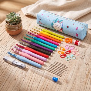 May include: A crochet hook set featuring multiple colorful hooks with ergonomic handles, a light blue pencil case with a tropical plant print, a white measuring tape, plastic stitch markers, a row counter, and a clear tube with metal needles.