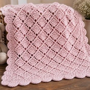 May include: A light pink crochet blanket featuring a repeating diamond pattern with openwork details and a scalloped edge. The textile is crafted with a soft yarn, showcasing a delicate texture and a consistent stitch throughout the entire piece.