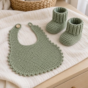 Può includere: Una bavaglino per neonati all'uncinetto color verde salvia con bordo smerlato e chiusura con bottone in legno, abbinato a un paio di scarpine all'uncinetto color verde salvia con polsino a coste. Il set è realizzato in filato testurizzato.