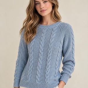 May include: A light blue long-sleeve sweater featuring a vertical cable knit pattern on the front and sleeves, a round crew neckline, and ribbed cuffs and hem. The knit texture is consistent throughout the garment, providing a structured look.