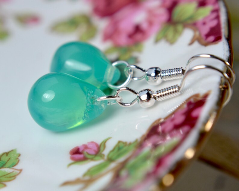 May include: A pair of silver teardrop earrings with light green glass drops.