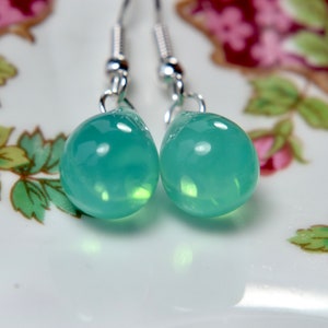 May include: A pair of silver dangle earrings with teardrop-shaped green gemstone pendants.