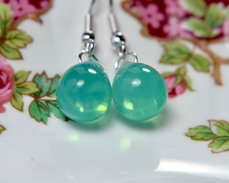 May include: A pair of silver dangle earrings with teardrop-shaped green gemstone pendants.