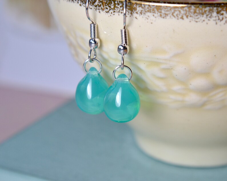 May include: A pair of silver teardrop earrings with light blue gemstone drops.