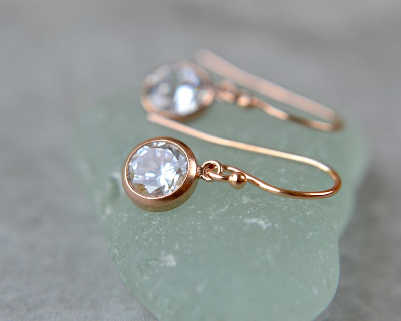 Puede incluir: Un par de pendientes de oro rosa con una piedra redonda transparente. Los pendientes tienen un dise&ntilde;o simple y elegante, perfectos para el uso diario.