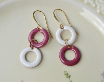 May include: A pair of dangle earrings with two circles on each earring. The top circle is pink and the bottom circle is white. The earrings are made of gold.