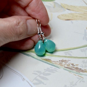 May include: A pair of silver dangle earrings with teardrop-shaped light blue gemstones.