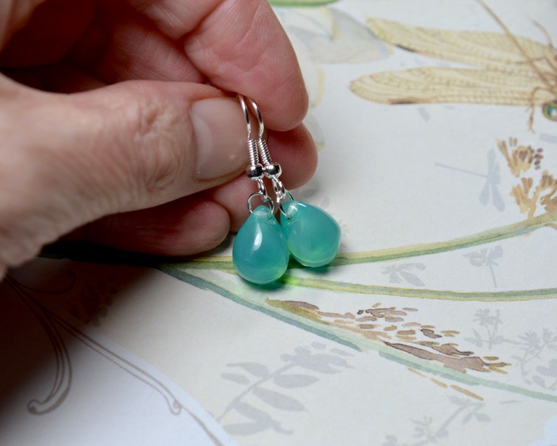 May include: A pair of silver dangle earrings with teardrop-shaped light blue gemstones.