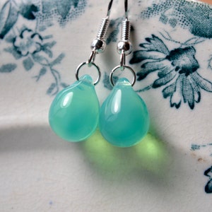 May include: A pair of silver teardrop earrings with light blue glass drops.